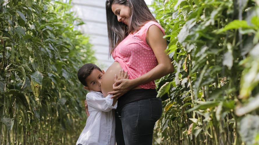 一名孕妇带着孩子站在植物田里