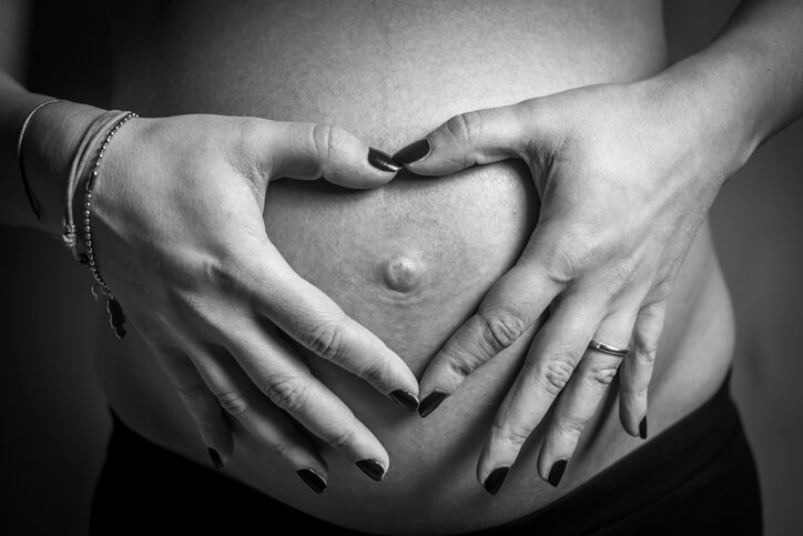 照片显示一名妇女怀孕的腹部，双手呈心形。